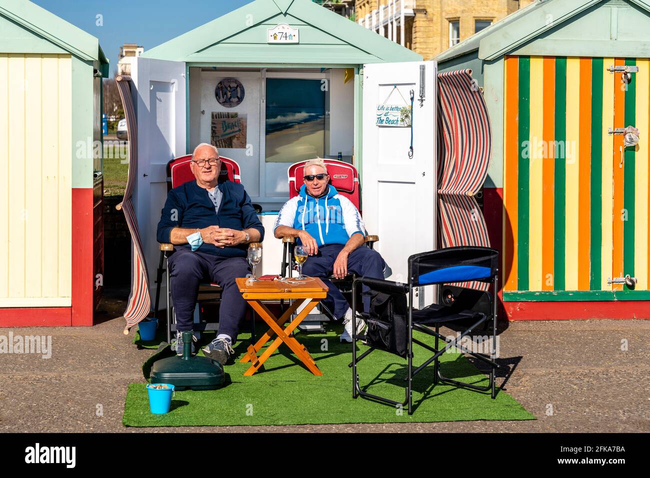 Deux hommes locaux appréciant le soleil à l'extérieur D'UNE cabane de plage sur le front de mer de Hove, Brighton, East Sussex, Royaume-Uni. Banque D'Images