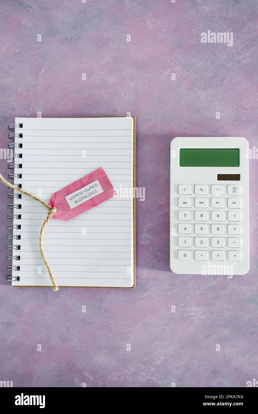 étiquette d'affaires pour femmes avec calculatrice et bloc-notes sur bureau rose, soutenant l'égalité et l'égalité des chances Banque D'Images