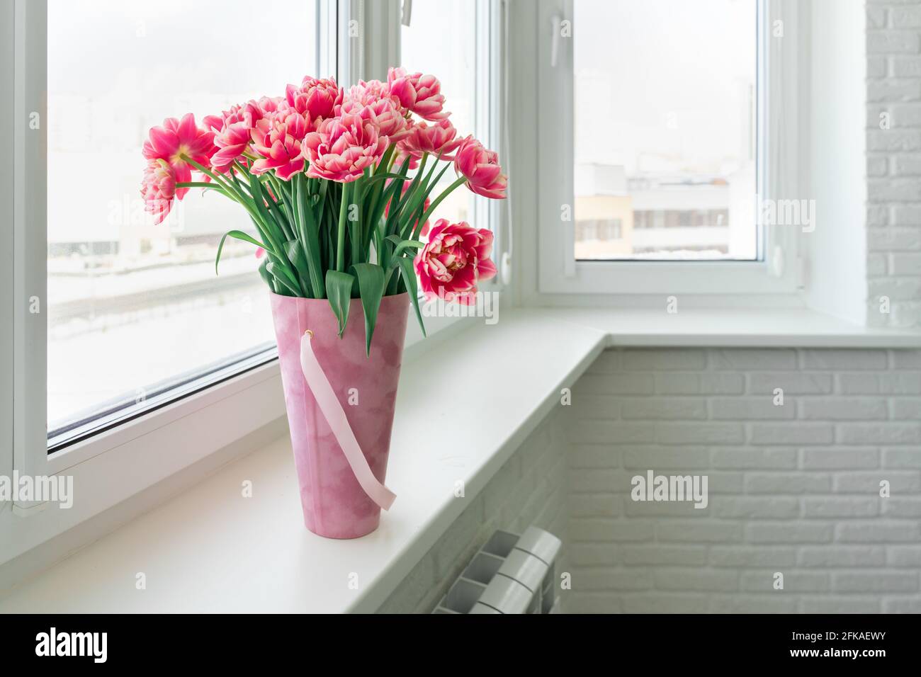 tulipes en terre rose dans un support de panier sur le rebord de la fenêtre. Banque D'Images