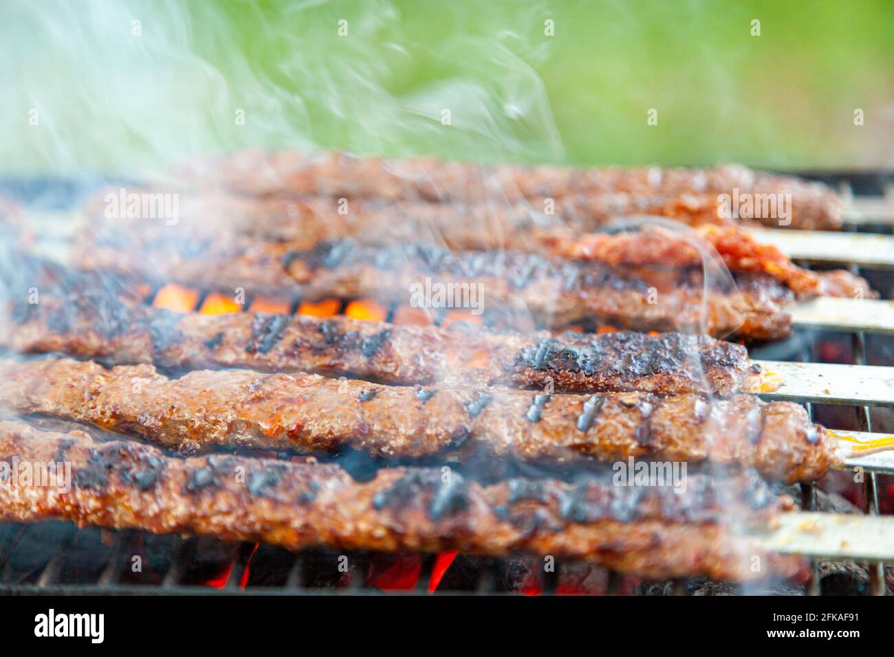 Cuisson de délicieux Adana Kebab turc sur un grill portatif au charbon de bois à un endroit de pique-nique, la fumée et la flamme s'échappe de la viande qui grésilte. Koftes sont li Banque D'Images