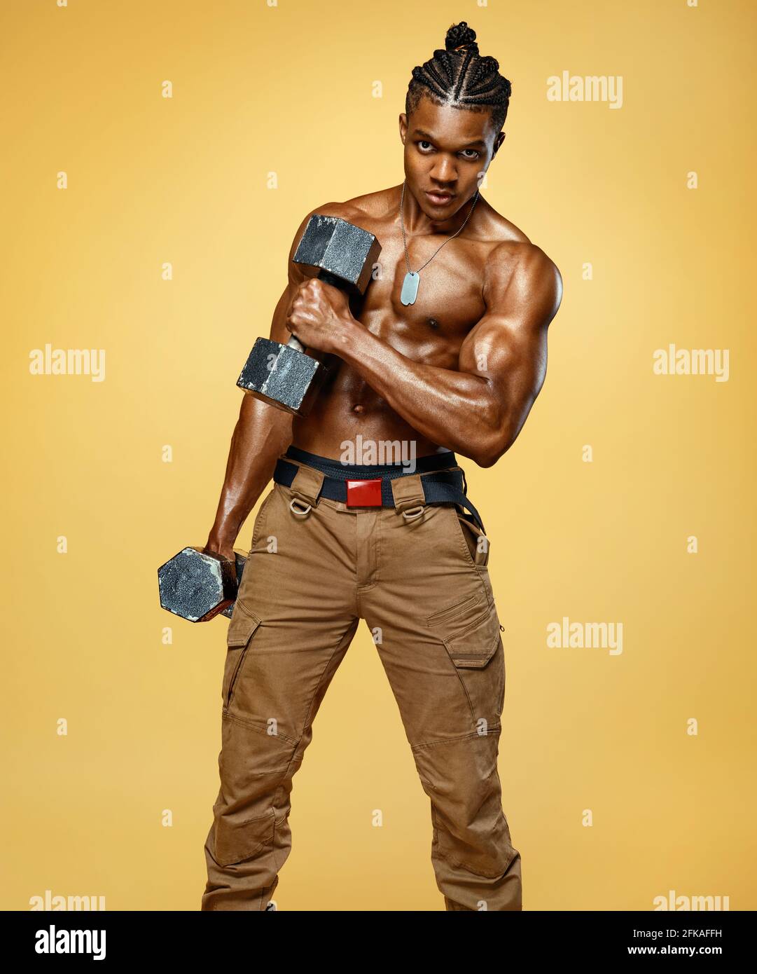 Homme fort faisant des exercices avec des haltères. Photo d'un homme musclé avec torse nu sur fond jaune. Force et motivation Banque D'Images