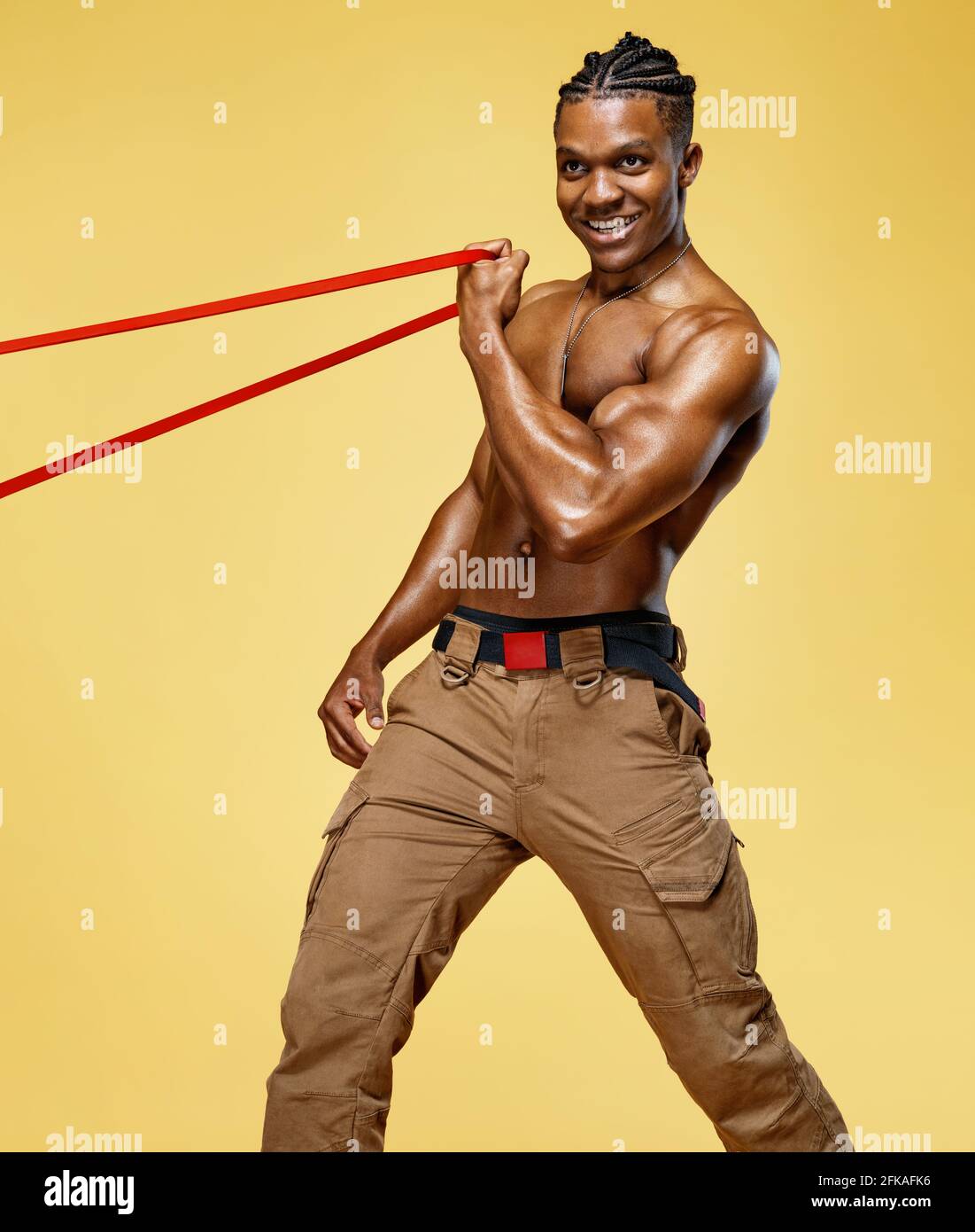 L'homme sportif effectue des exercices en utilisant la bande de résistance. Photo de l'homme afro-américain sur fond jaune. Force et motivation Banque D'Images