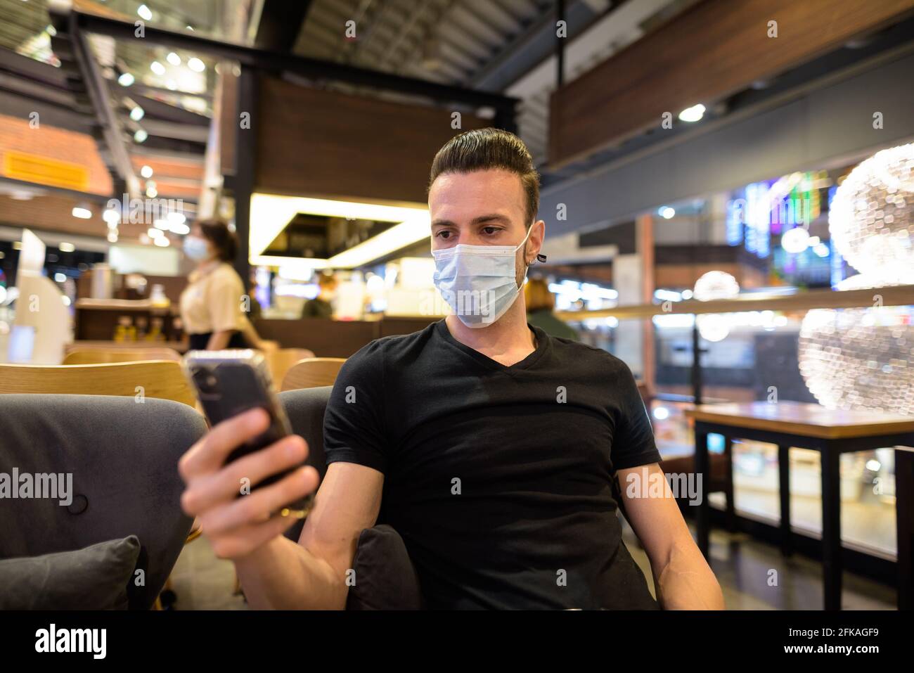 Homme assis au café tout en sociant et en utilisant téléphone portable et port de masque Banque D'Images