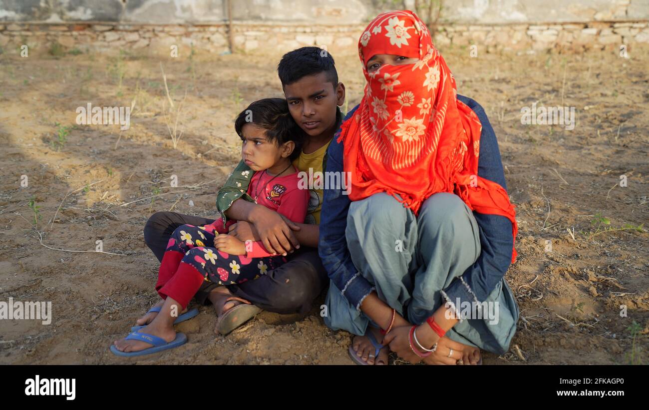 08 avril 2021- Reengus, Sikar, Inde. Une jeune fille a masqué son visage et s'est assise sur terre avec son petit frère et sa sœur. Petite fille indienne rurale Banque D'Images