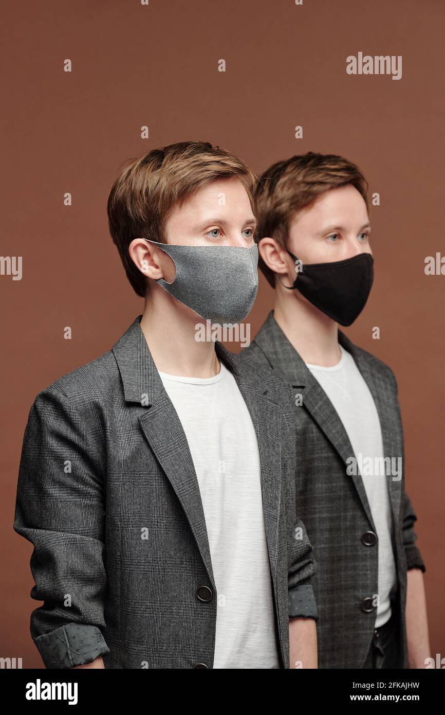 Rangée de jeunes jumeaux doués en costume gris et masques en tissu qui travaillent dans le domaine des affaires Banque D'Images
