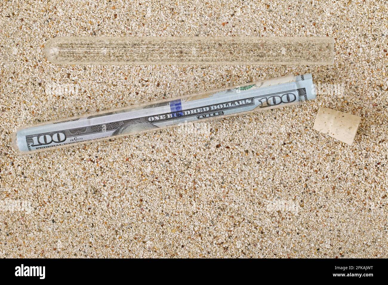 Un rouleau ou nouveau billet de 100 dollars américains à l'intérieur d'un Tube avec couvercle en liège retiré sur une plage de sable message dans un style bouteille Banque D'Images