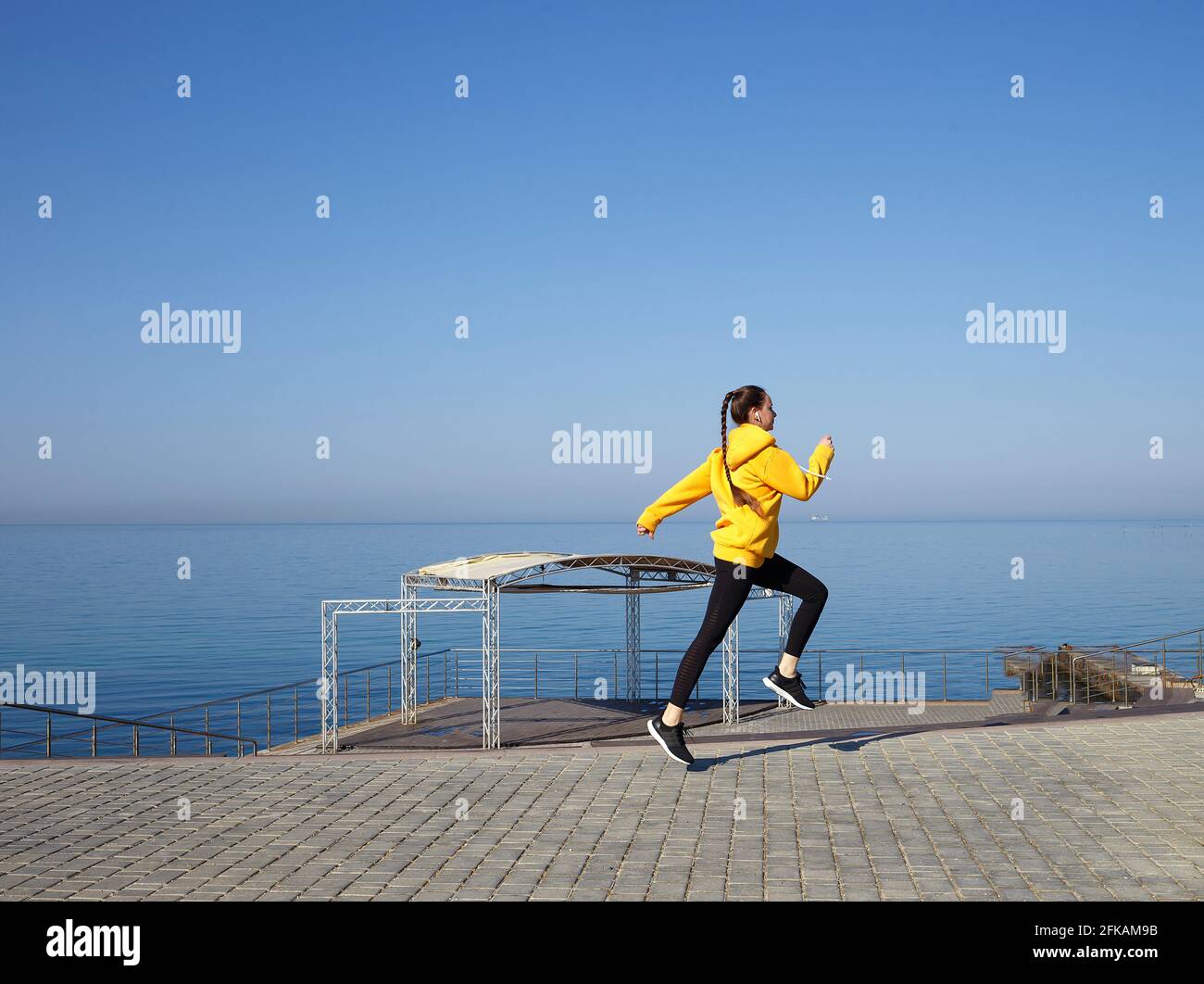 jeune femme en pull à capuche jaune au bord de la mer. Banque D'Images