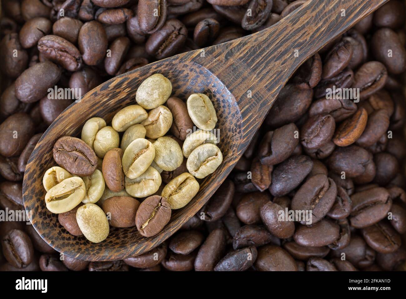 Cuillère de graines de café vert non torréfiées séchées sur dessus de grains de café torréfiés Banque D'Images