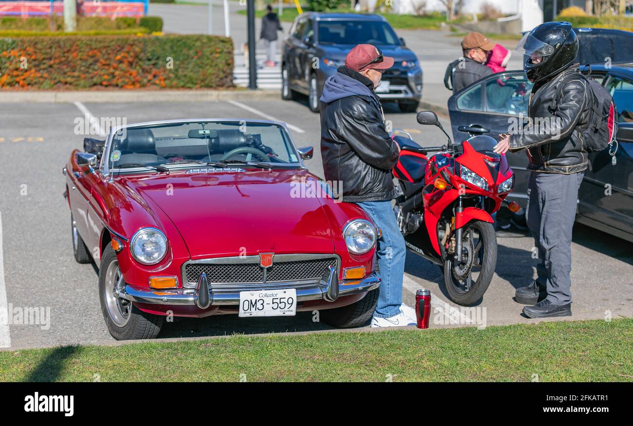 Deux vieux qui parlent devant une voiture dans un parking de rue. Une avec la moto et une avec la voiture rouge vintage. Banque D'Images