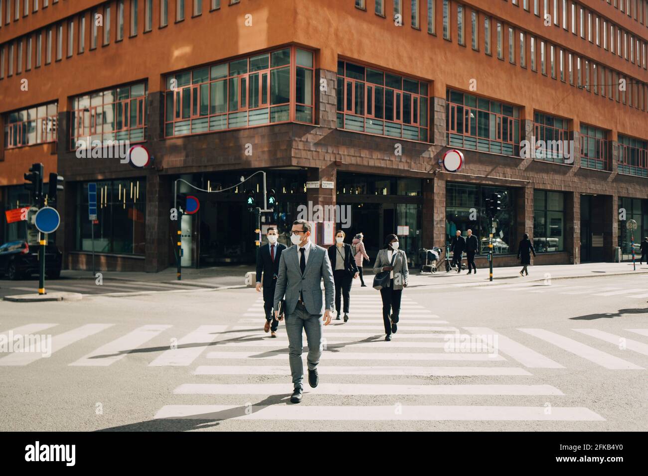 Les gens d'affaires traversent la rue le jour ensoleillé pendant la COVID-19 Banque D'Images