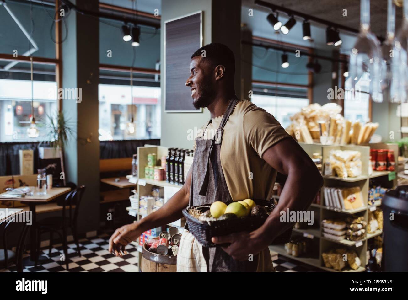Jeune homme propriétaire debout avec un panier de fruits dans un magasin de charcuterie Banque D'Images