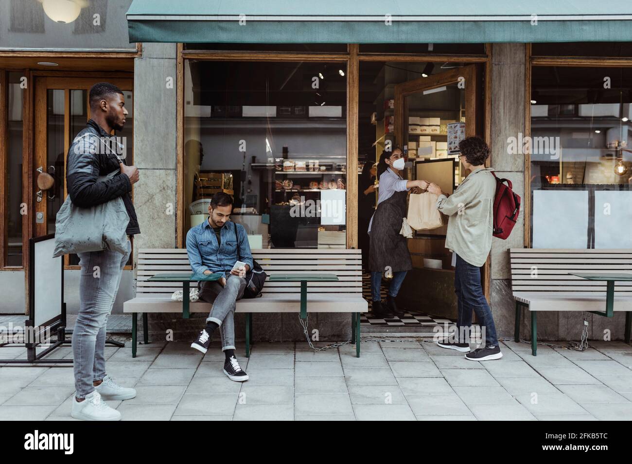 Les clients qui maintiennent leur distance sociale tout en recueillant leur commande dans un magasin de charcuterie pendant une pandémie Banque D'Images