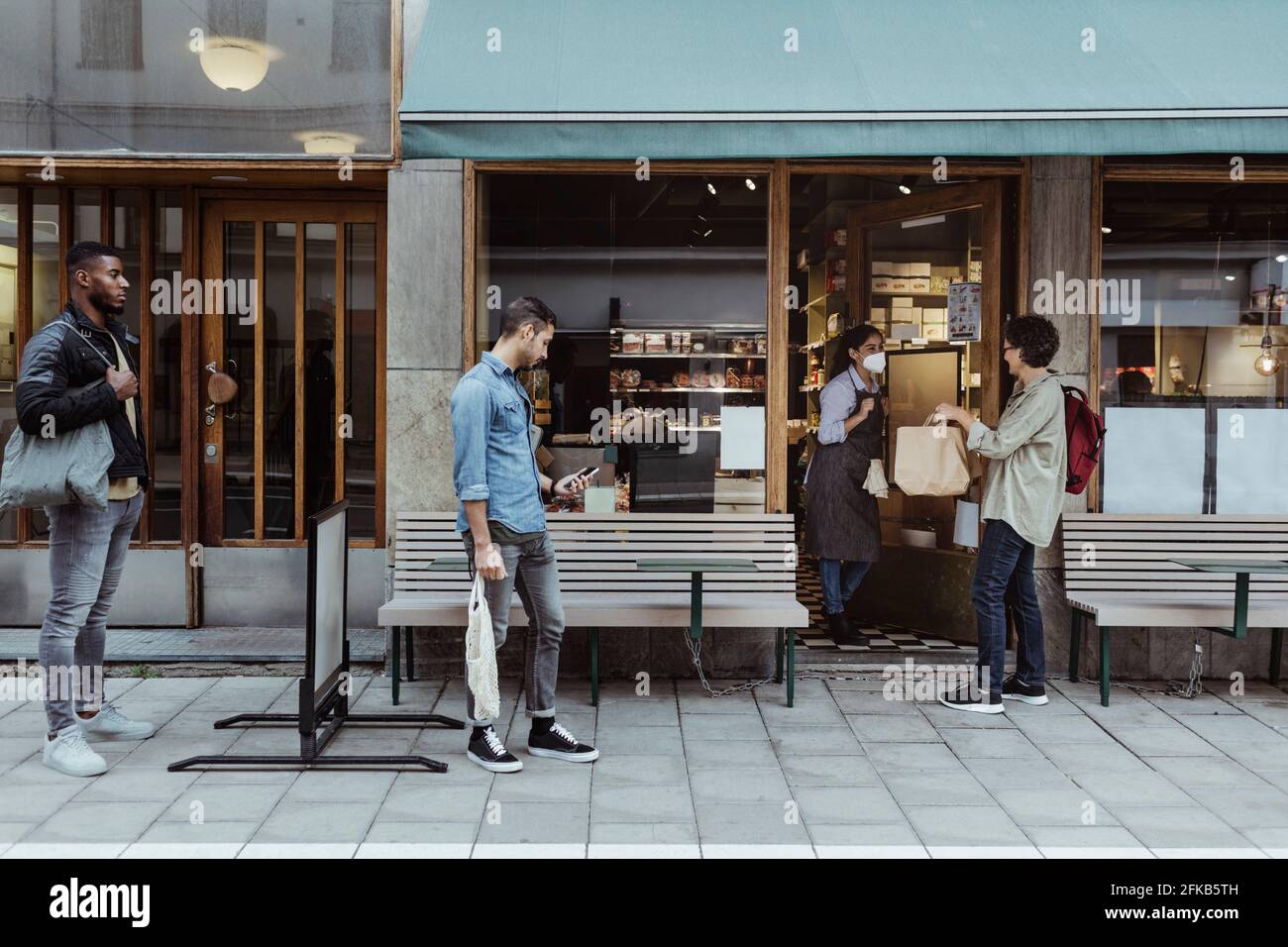 Les clients qui maintiennent leur distance sociale tout en recueillant leur commande dans une épicerie fine Banque D'Images