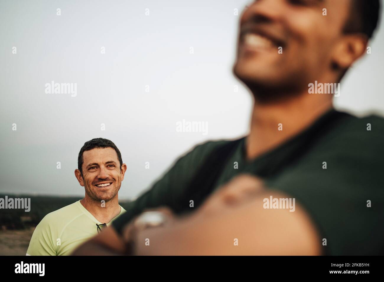 Sportif souriant regardant l'athlète masculin contre le ciel pendant le coucher du soleil Banque D'Images