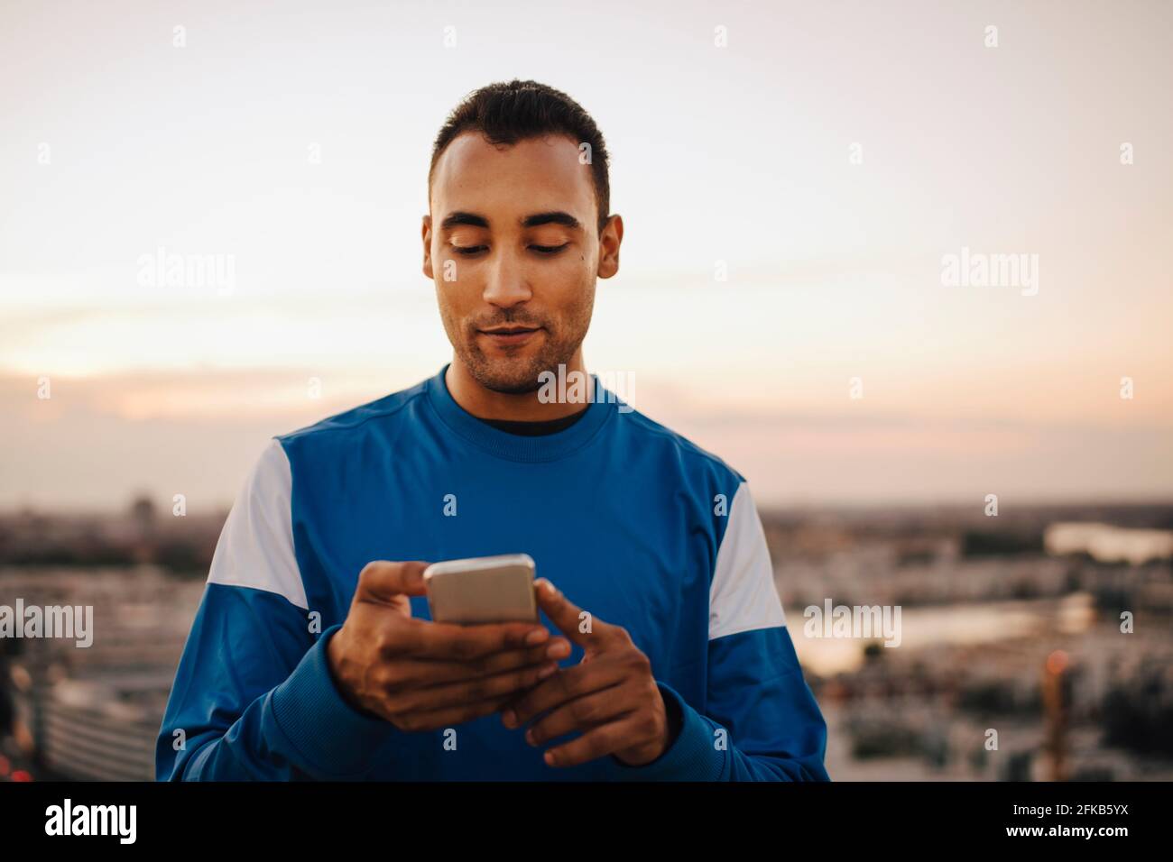 Sportif utilisant un smartphone contre le ciel pendant le coucher du soleil Banque D'Images