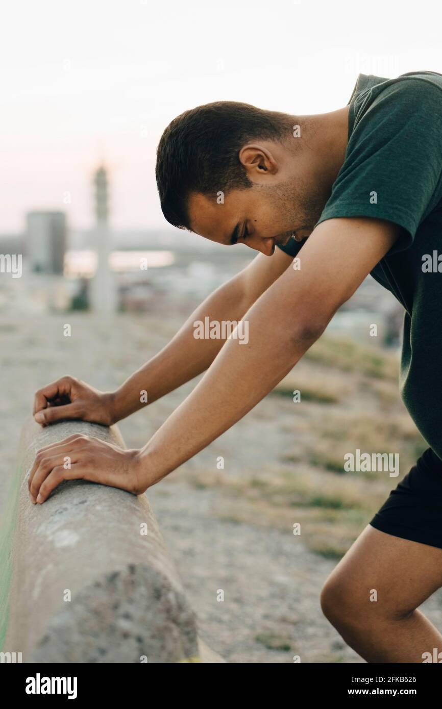 Jeune athlète masculin s'appuyant sur le mur de soutènement pendant le coucher du soleil Banque D'Images