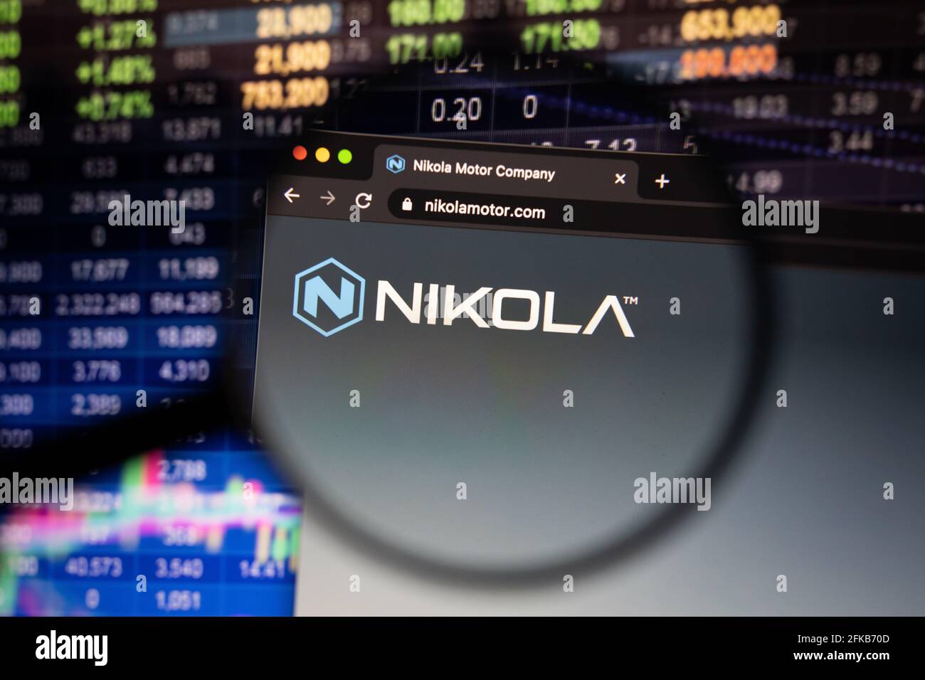 Logo de la société Nikola sur un site Web avec des développements flous de marché boursier en arrière-plan, vu sur un écran d'ordinateur par une loupe Banque D'Images