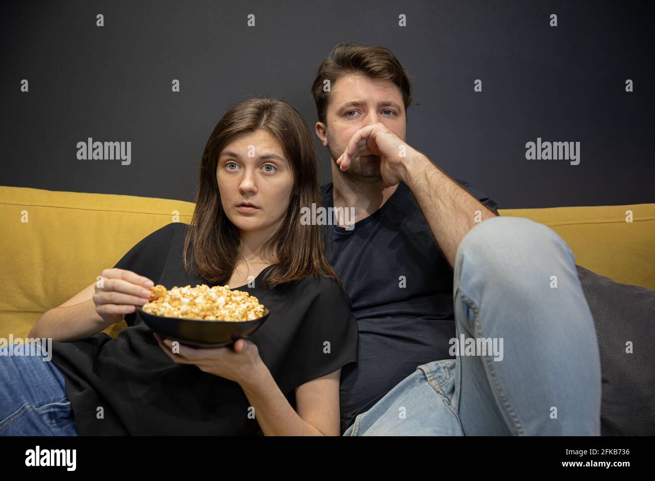 Couple regardant un film télé se portant allongé sur un canapé en train de manger du pop-corn à la maison Banque D'Images