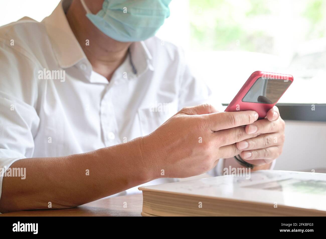 Homme avec masque de visage assis à côté des fenêtres de SMS sur son téléphone. Vue en gros plan. Banque D'Images