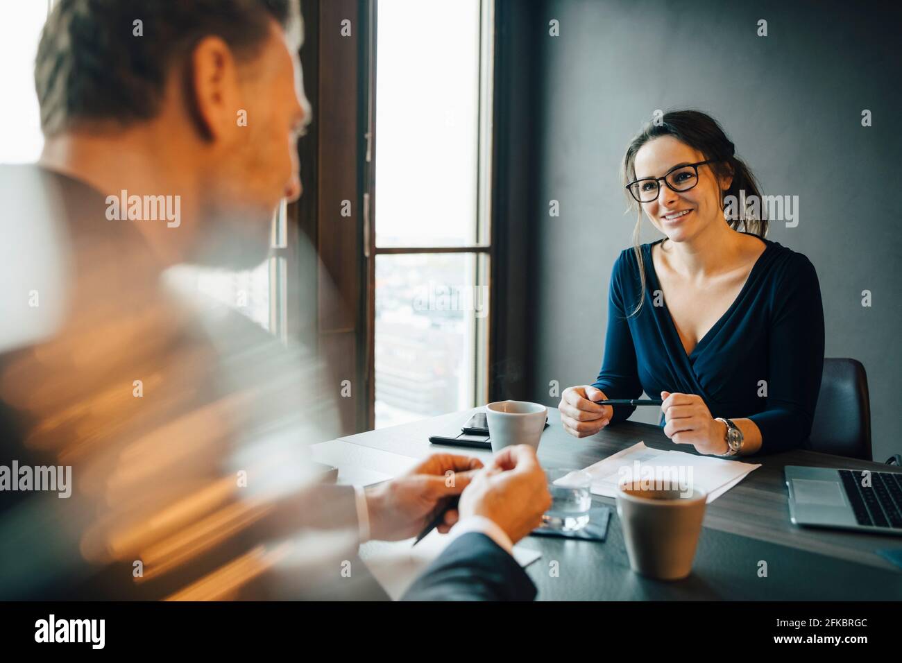 Femme d'affaires souriante discutant avec un collègue dans la salle du conseil d'administration de bureau Banque D'Images