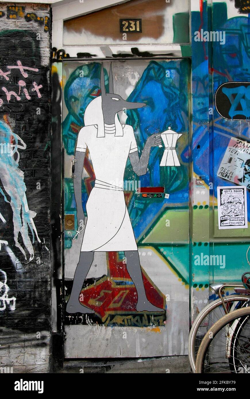 Étrange brew … Anubis, l'ancien dieu de la mort et de l'après-vie à tête de chacal égyptien, porte une cafetière dans cet art psychédélique de rue peint sur une porte d'un ancien fief de squatters à long terme près du célèbre Slangenhuis ou Snake House à Spuistraat, Amsterdam, Hollande du Nord, pays-Bas. Bien que les sans-abri, les artistes et les musiciens qui ont occupé des propriétés vides ici pendant des années soient maintenant partis depuis longtemps, la région de Spuistraat attire encore de nouvelles générations de touristes désireux de profiter des étonnantes œuvres d'art urbaines qu'ils ont laissées derrière eux. Banque D'Images