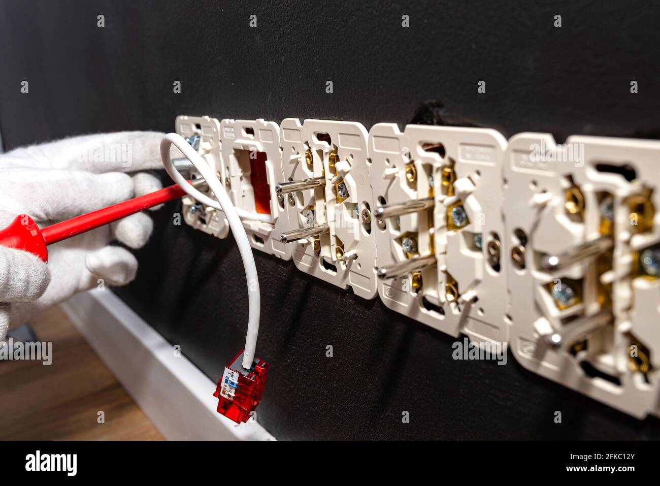 Un câble réseau dépassant du mur avec un module RJ45 prêt à l'emploi vers la prise de l'ordinateur dans la salle, prises électriques visibles. Banque D'Images