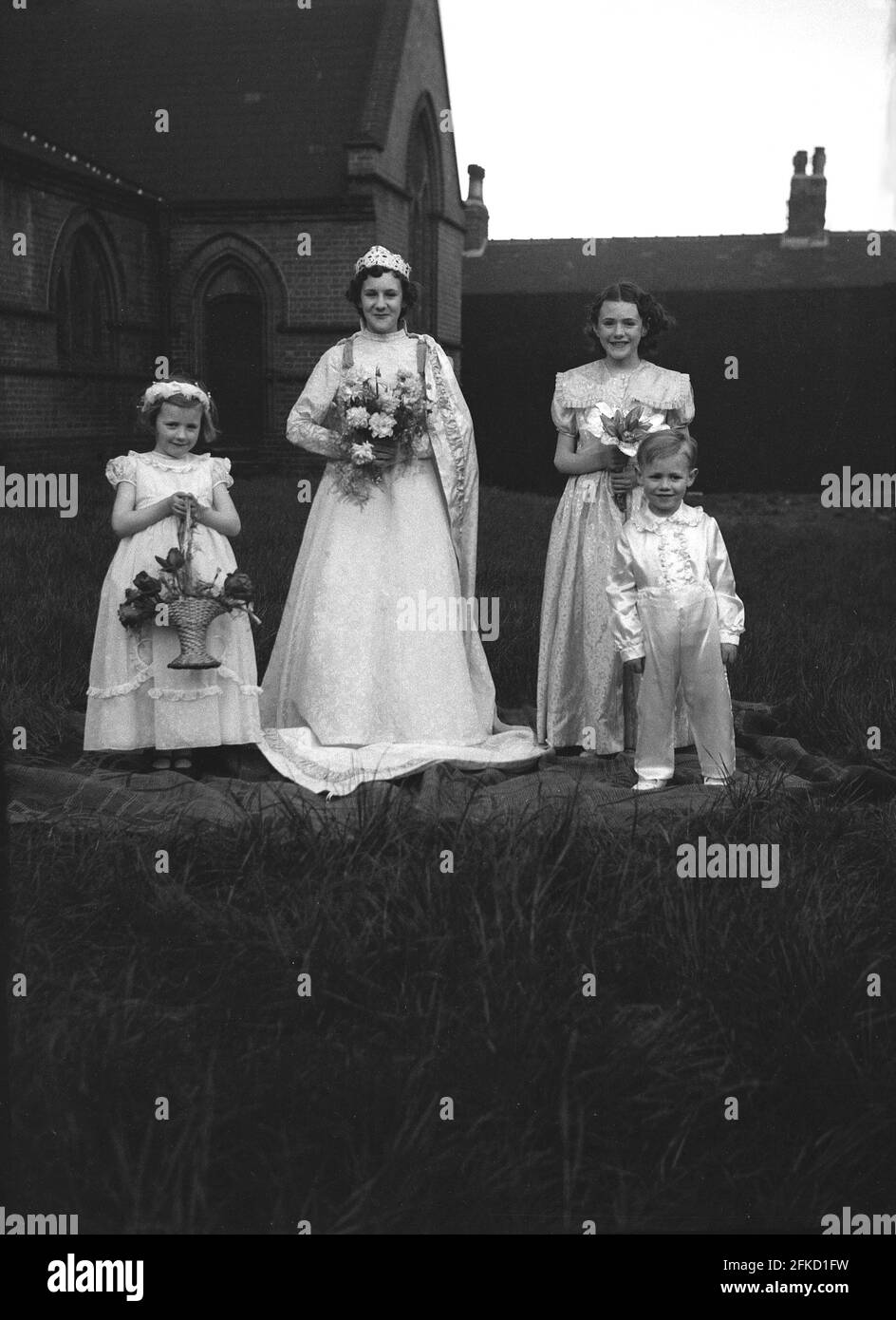 1958, historique, le Carnaval de la Reine de mai, la Reine de mai locale et trois autres jeunes enfants en costumes qui participent aux célébrations, se tiennent sur un tapis à l'extérieur d'une église pour leur photo. Le jour de mai était une tradition ancienne qui célébrait l'arrivée du printemps et de l'été. Dans de nombreuses villes britanniques du nord, le défilé était relié à l'école du dimanche de l'Église d'Angleterre. La figure de la reine de mai et sa pureté sont liées au culte et au folklore anciens. Banque D'Images