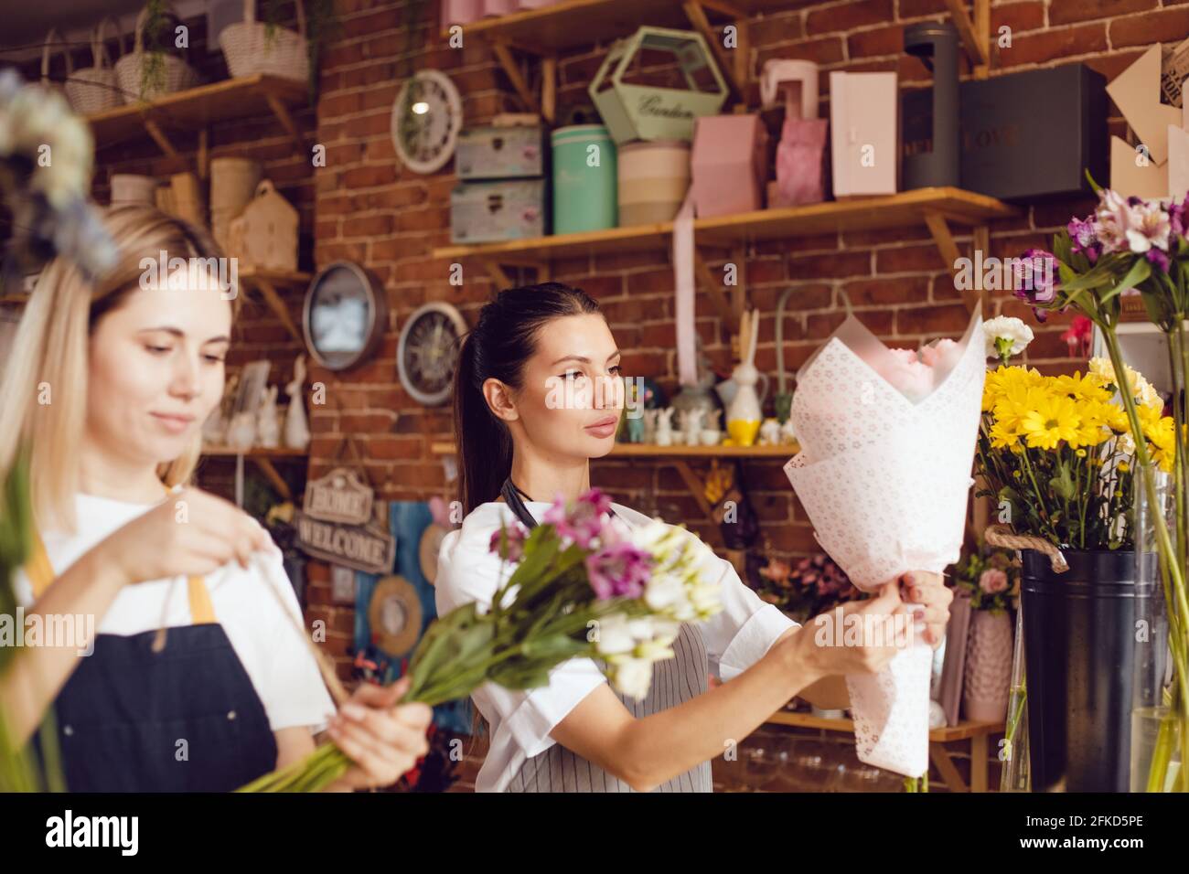 Femme fleuriste avec assistant collectent des bouquets dans un fleuriste. Banque D'Images