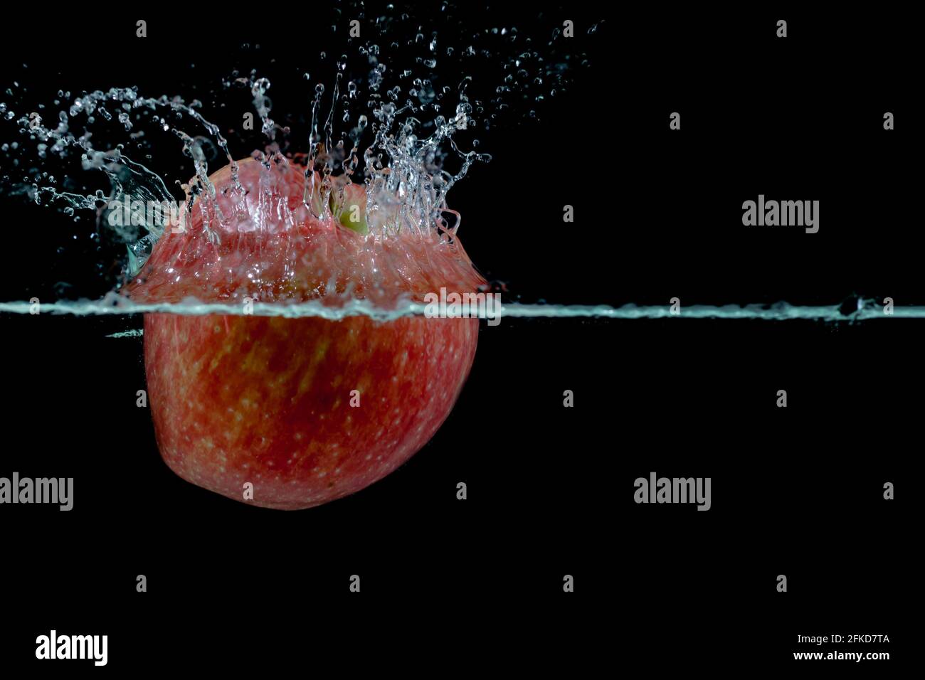 la pomme rouge tombe dans l'eau avec des éclaboussures sur fond noir, placez sous le texte Banque D'Images