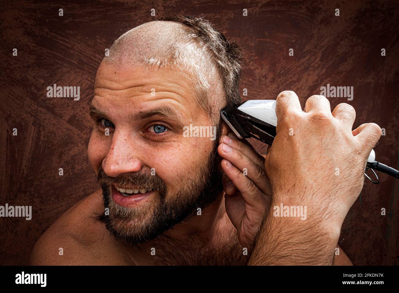 Homme caucasien essayant de se raser la tête avec un rasoir électrique. Un  chauve brutal tient un rasoir dans la main et rasse le chaume sur un fond  métallique Photo Stock -