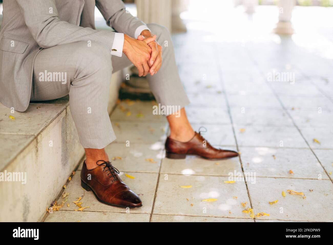 Un homme dans un costume gris et des chaussures marron en cuir s'assoit sur  la marche avec ses mains pliées Photo Stock - Alamy
