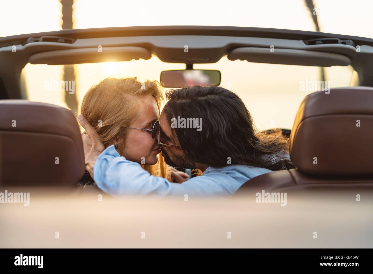 Couple heureux embrassant en voiture convertible - personnes romantiques ayant un moment tendre pendant le voyage en voiture dans la ville tropicale Banque D'Images