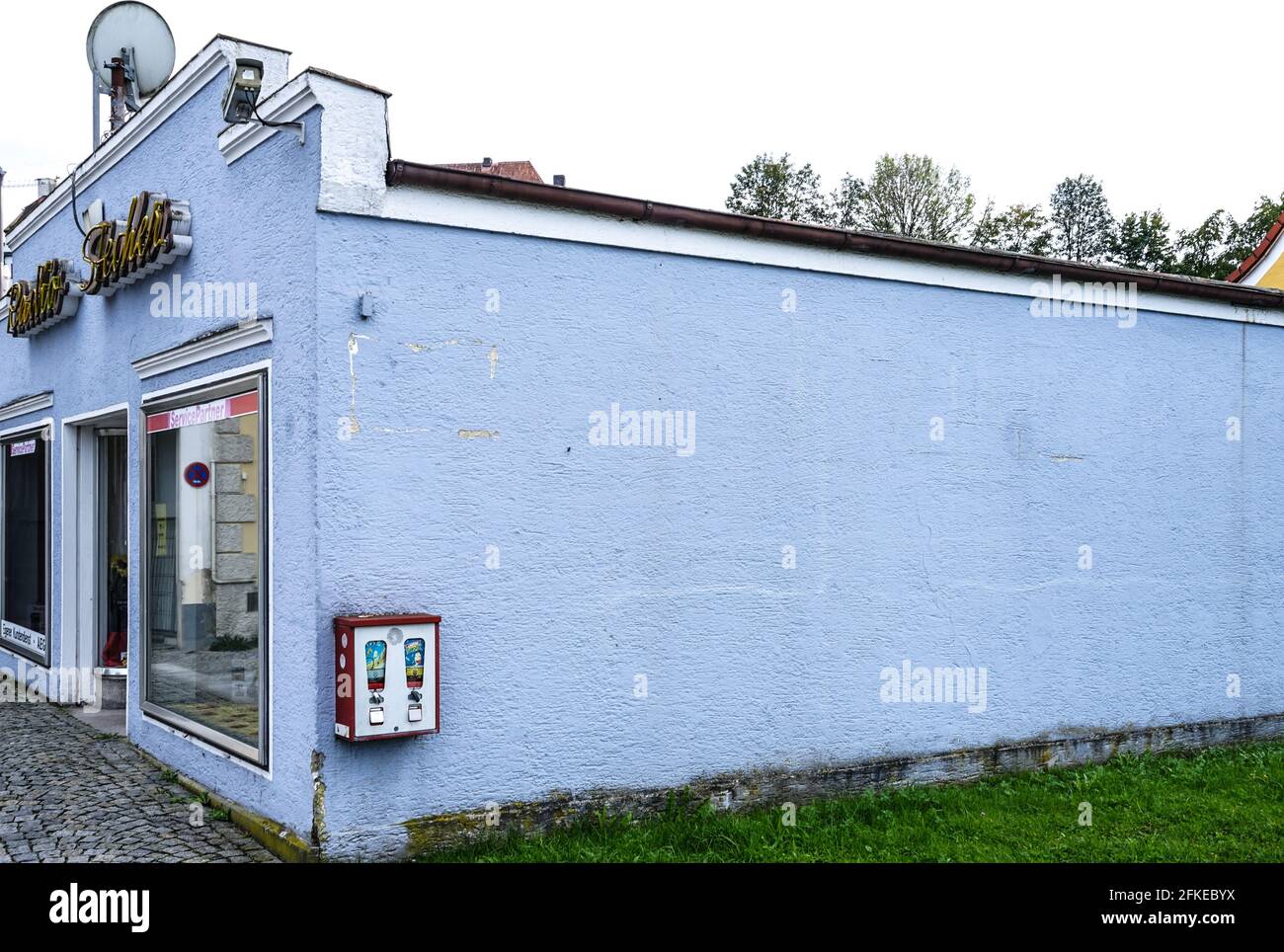 Vue sur une maison avec un long mur latéral sur lequel est suspendue une vieille machine à mâcher des gencives. Banque D'Images