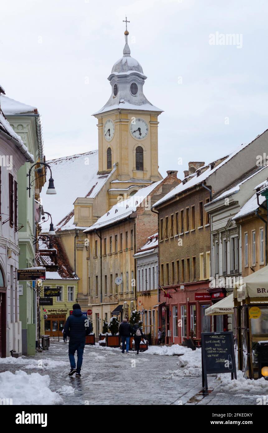 Les acheteurs au milieu de la neige printanière à Strada Michael Weiss, dans le centre historique de Brasov en Roumanie. L'église catholique de Biserica Sfintii Petru si Pavel i Banque D'Images