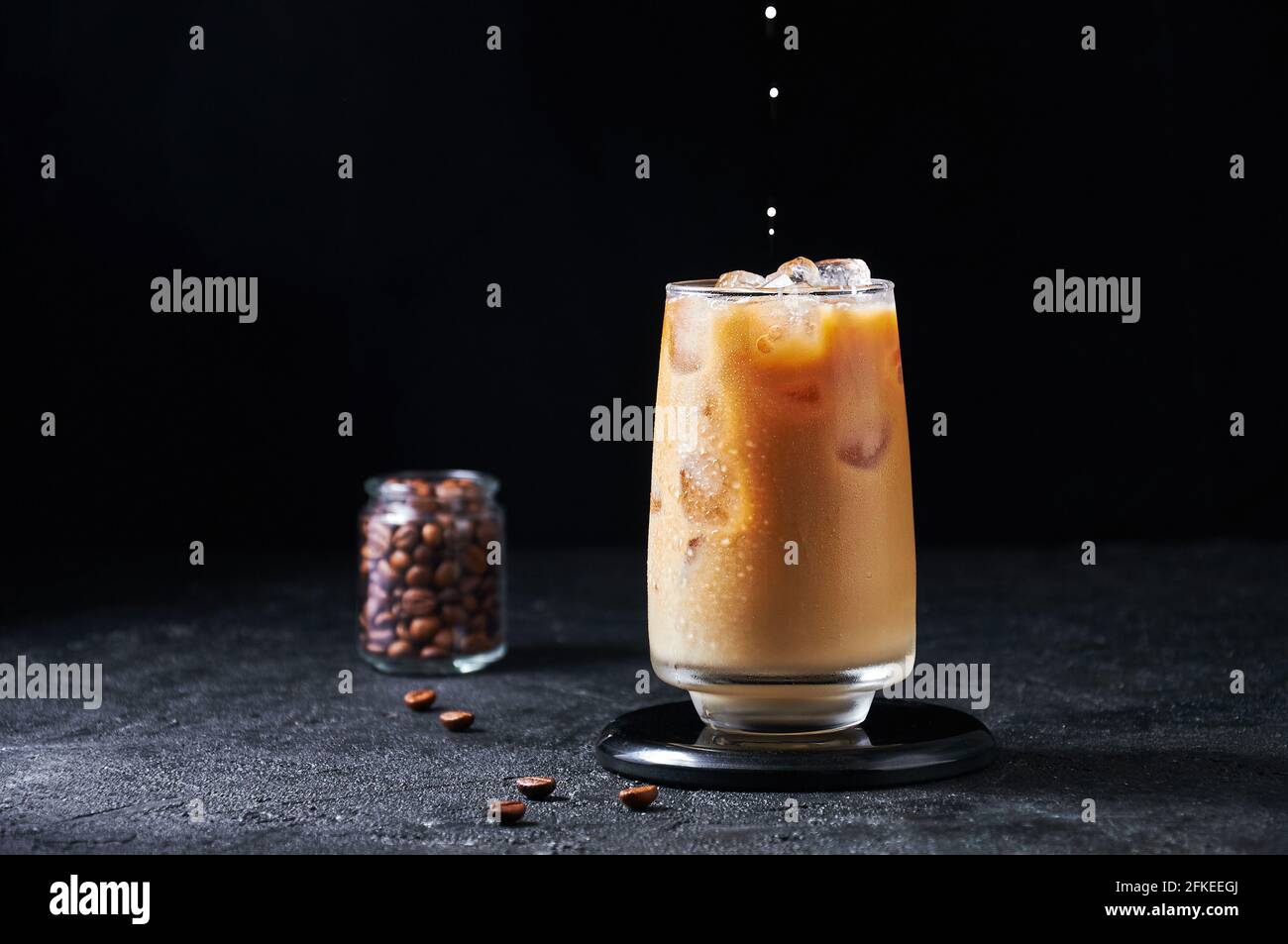 Le Lait Est Versé Dans Du Café Glacé Dans Le Grand Verre Sur Fond Sombre. Boisson D'Été Rafraîchissante Concept. Banque D'Images