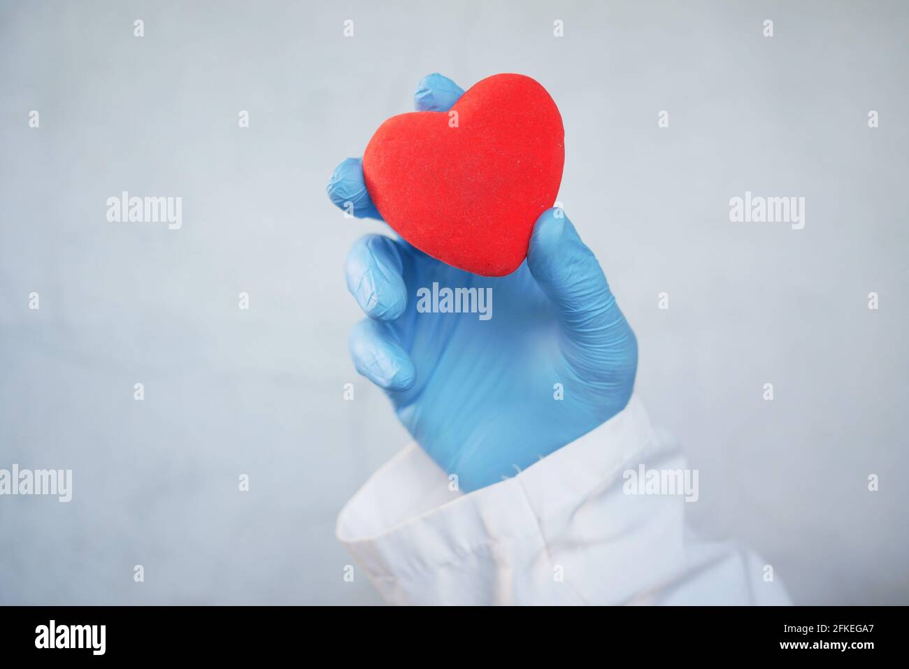 homme main dans des gants de protection tenant coeur rouge sur blanc arrière-plan Banque D'Images