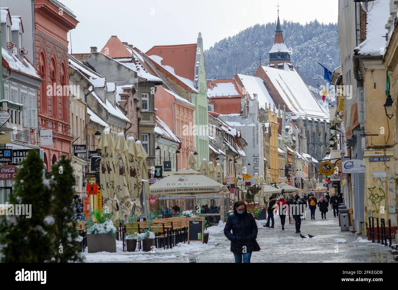 Les amateurs de shopping au milieu de la neige de printemps à Strada Republicii, dans le centre historique de Brasov en Roumanie. La célèbre église noire est importante en arrière-plan - pH Banque D'Images