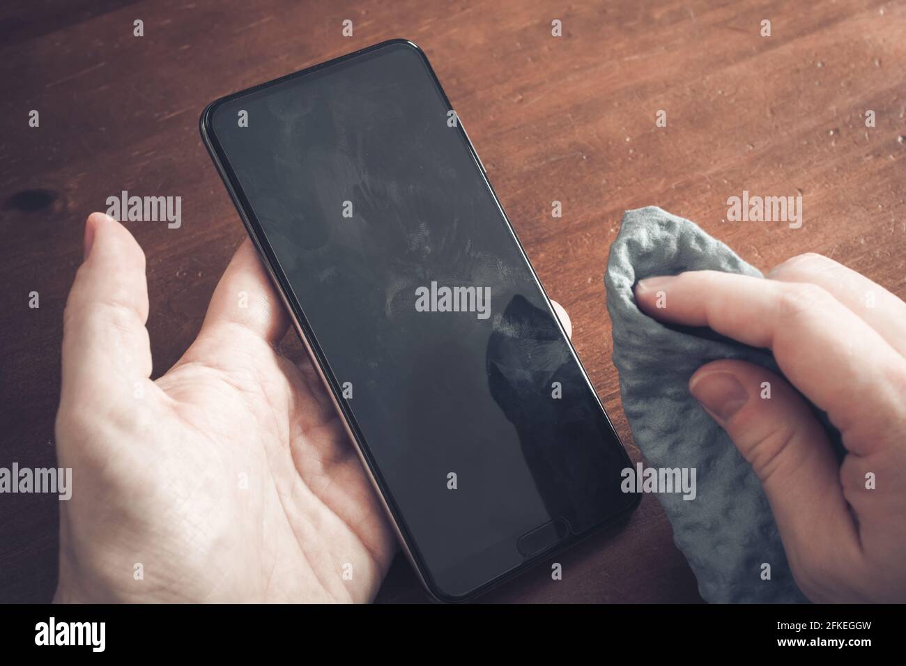 Nettoyage DE la poussière, de la saleté et des traces de doigts sur L'écran d'un smartphone à l'aide D'un chiffon de nettoyage sur UNE table Banque D'Images