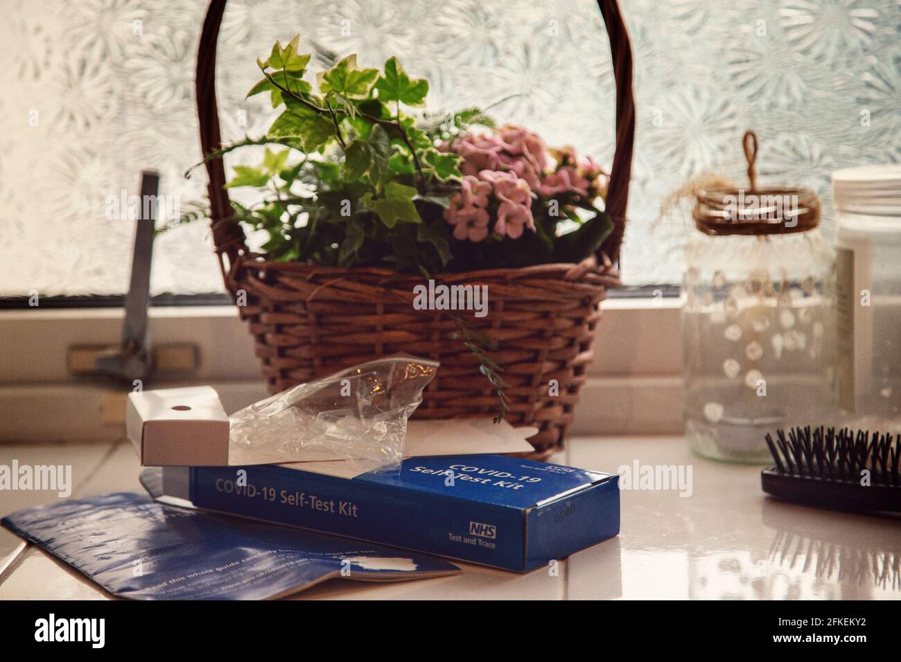 Covid 19 rapide d'auto-test sur une salle de bains carrelée avec des plantes de maison, des cheveux, des bocaux devant une fenêtre en verre texturé. Banque D'Images