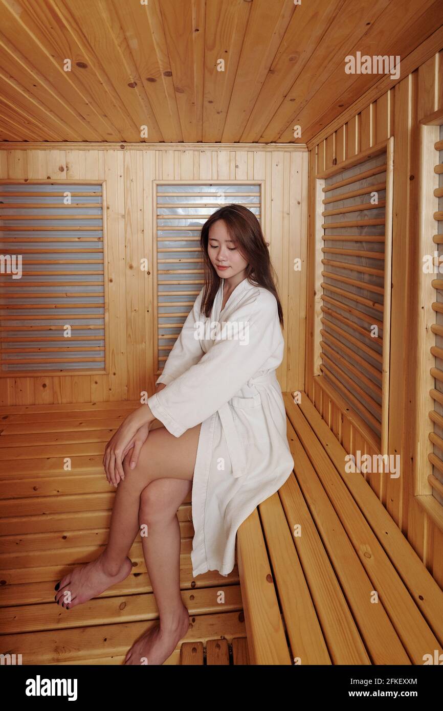 Jolie jeune femme asiatique en peignoir, assise sur le banc sauna chaud Banque D'Images