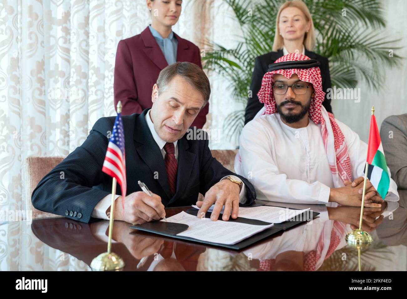 Un groupe de personnes assis à table pendant que l'un de ils signent un contrat après négociation Banque D'Images
