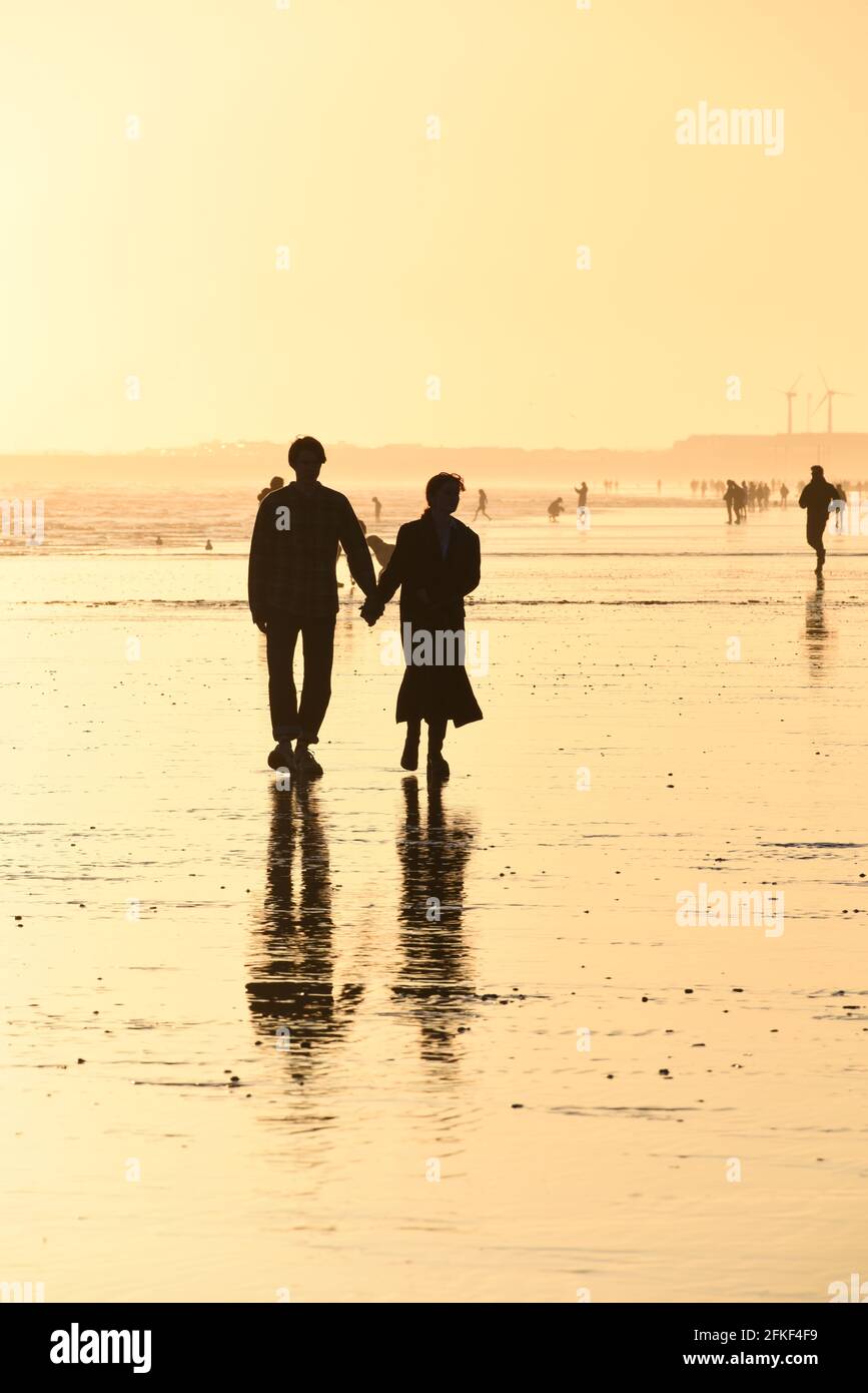 Un jeune couple marchant sur la plage de Hove, silhoueté au coucher du soleil Banque D'Images