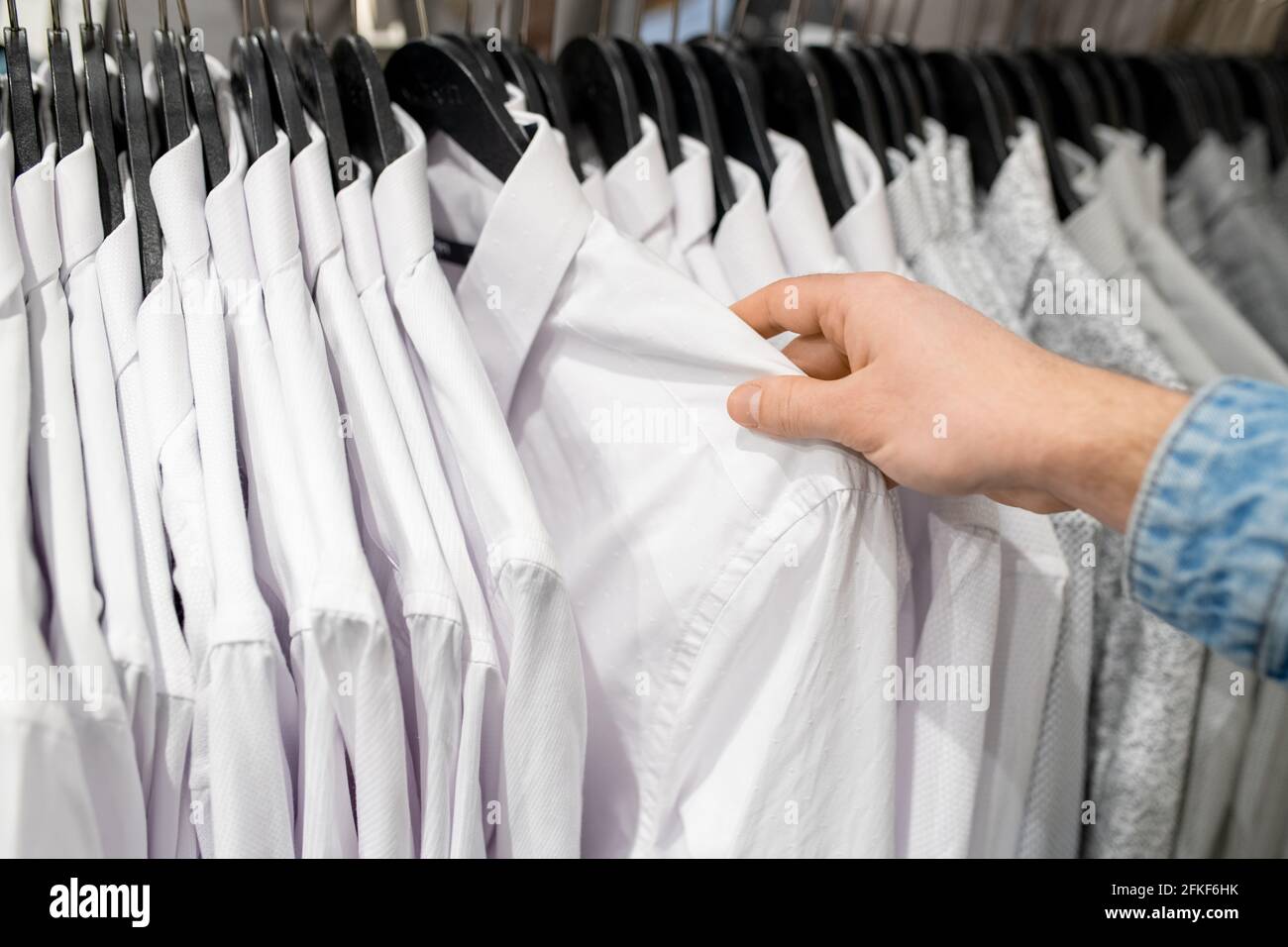Main de l'acheteur choisissant une chemise blanche dans le magasin de vêtements Banque D'Images