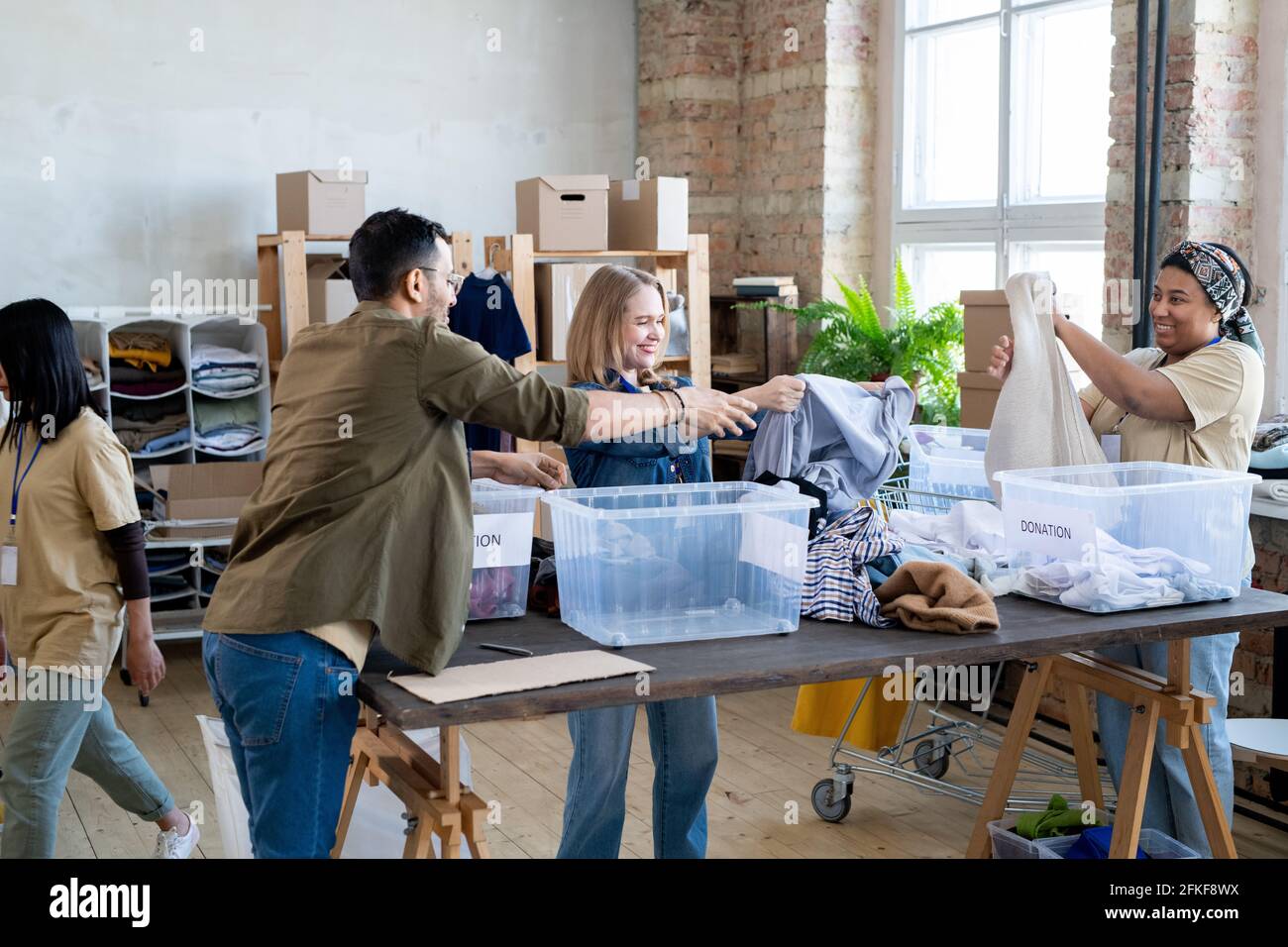 Les femmes heureuses choisissent des vêtements de don dans des récipients sur la table Banque D'Images