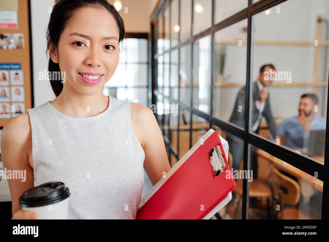 Portrait de jeune entrepreneur gaie avec presse-papiers et coupe de café dans le bureau de l'entreprise Banque D'Images