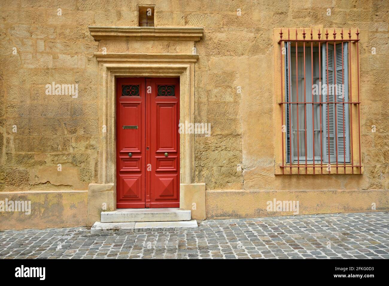 Façade de maison de style provençal avec un mur en stuc ocre, une porte rouge vif et une fenêtre avec des volets en bois à Aix-en-Provence Marseille, France. Banque D'Images