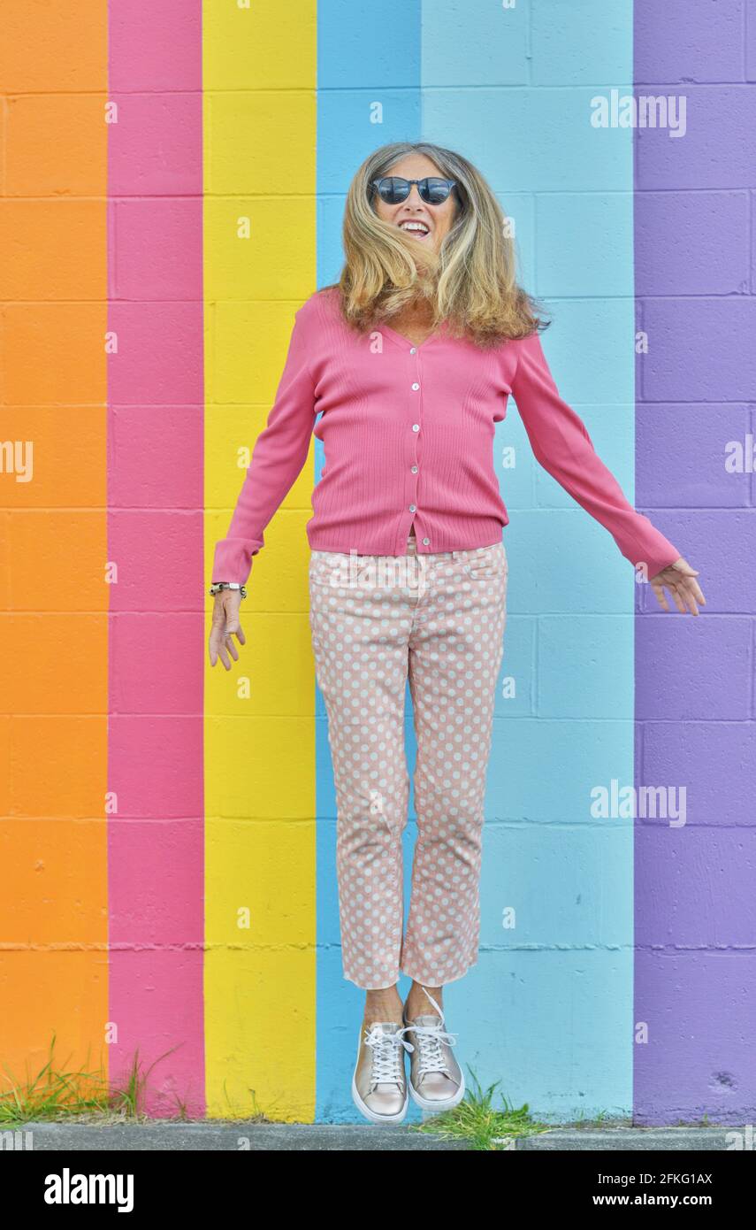 Belle femme sénior sautant sur un mur à rayures de couleurs vives en plein air Banque D'Images