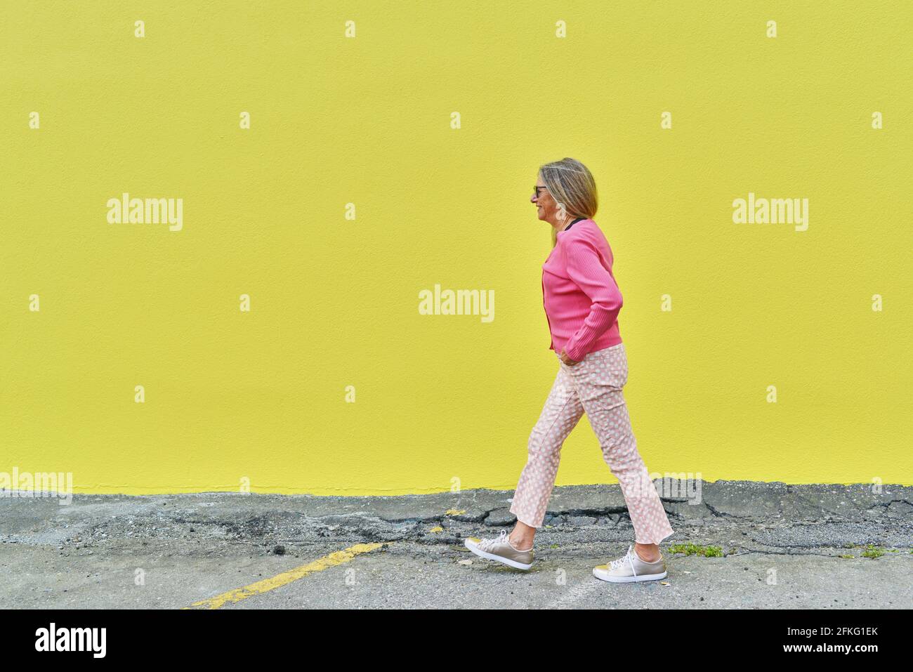 Belle femme âgée marchant sur un mur jaune vif à l'extérieur Banque D'Images
