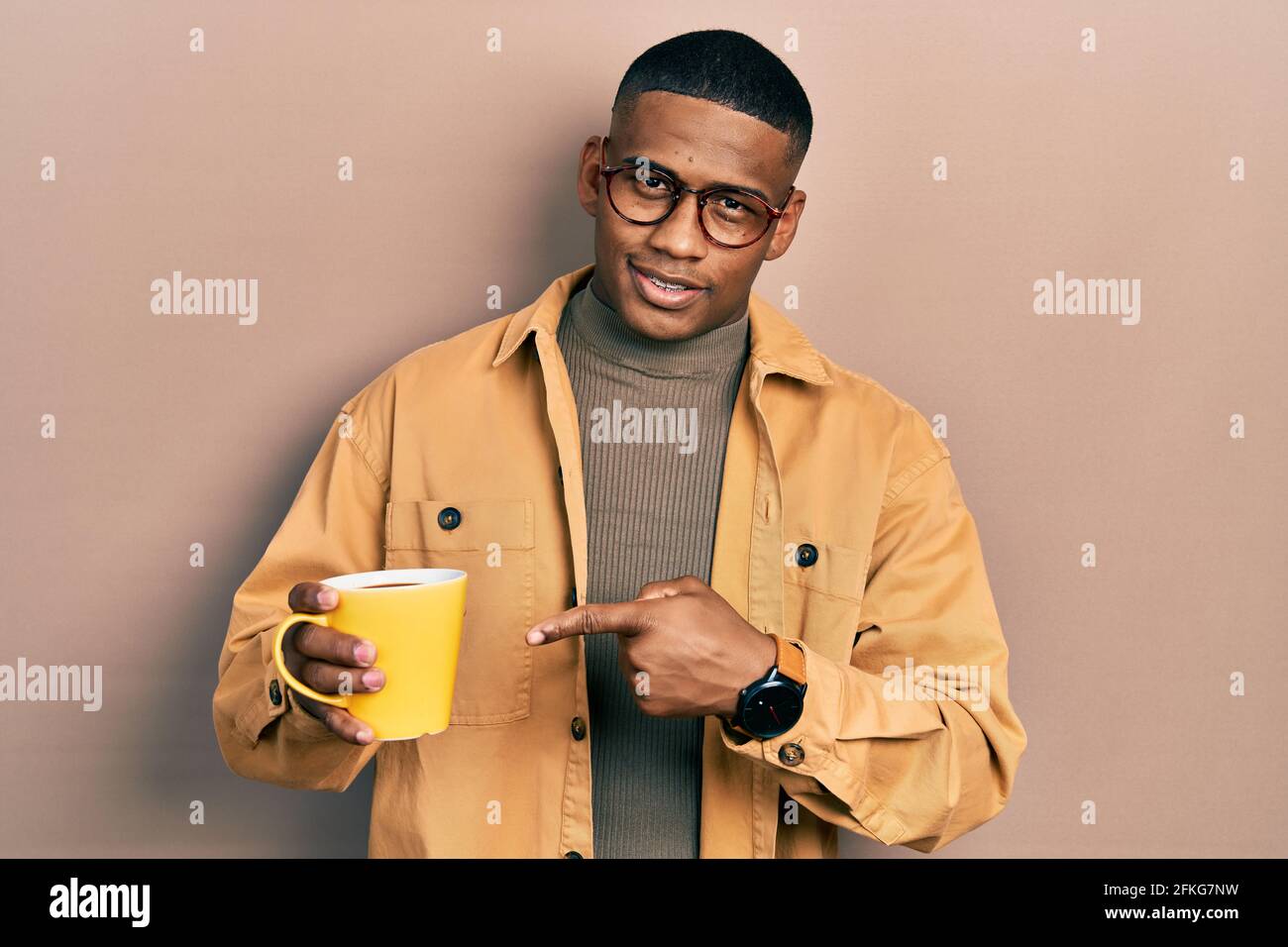 Jeune homme noir portant des lunettes et buvant une tasse de café souriant,  avec la main et le doigt Photo Stock - Alamy