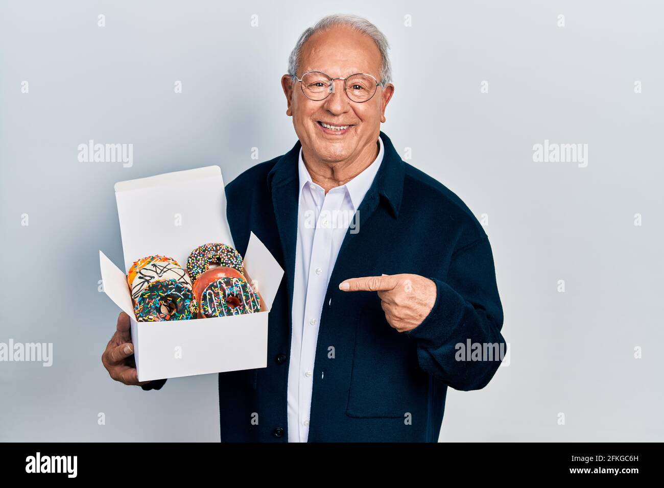 Homme âgé avec cheveux gris tenant pile de savoureux coloré boîte de beignets souriant, avec la main et le doigt Banque D'Images